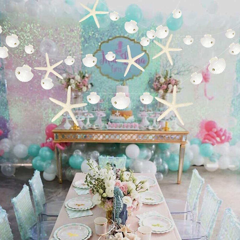 White starfish and seashell paper garland strung across a party setting with a dessert table and chairs.