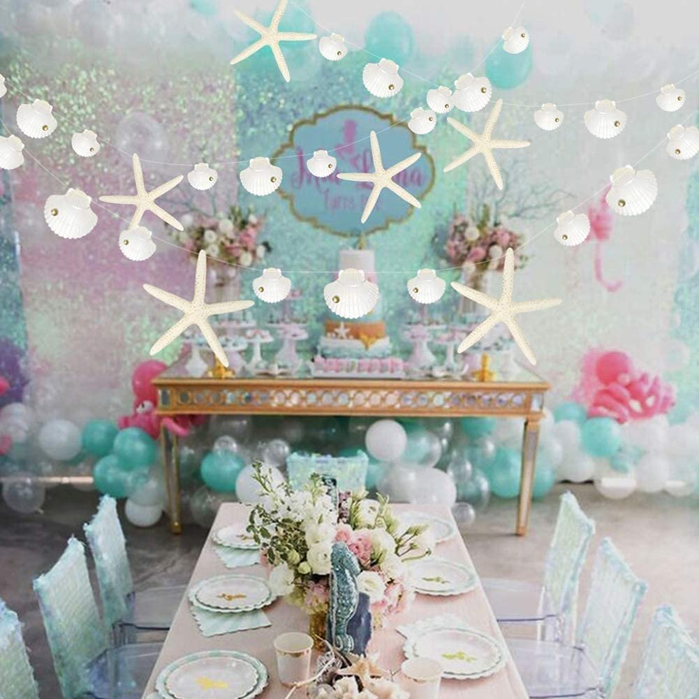 White starfish and seashell paper garlands strung across a party setting with a decorated table and balloons.