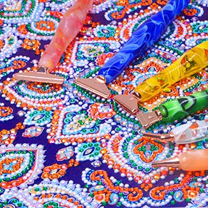 Diamond painting pens with rose gold tips resting on a colorful patterned canvas