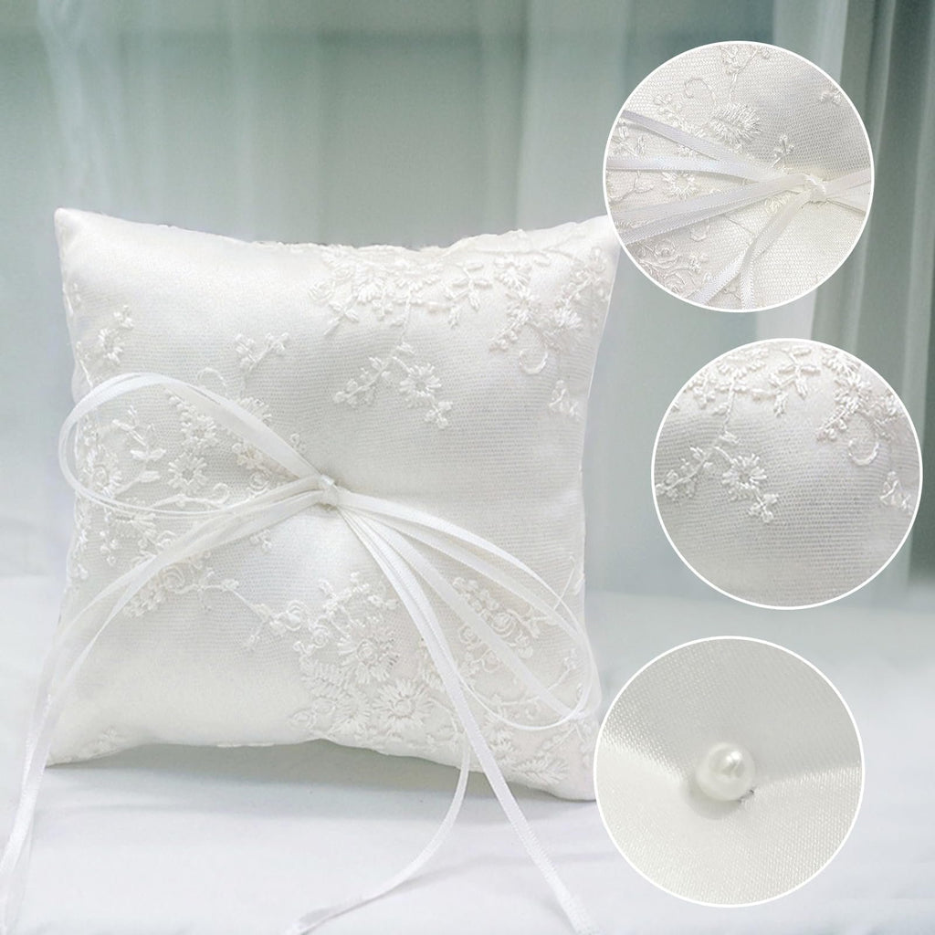 White satin ring bearer pillow with floral lace embroidery and ribbon bow, shown with close-up details of lace and pearl accent.