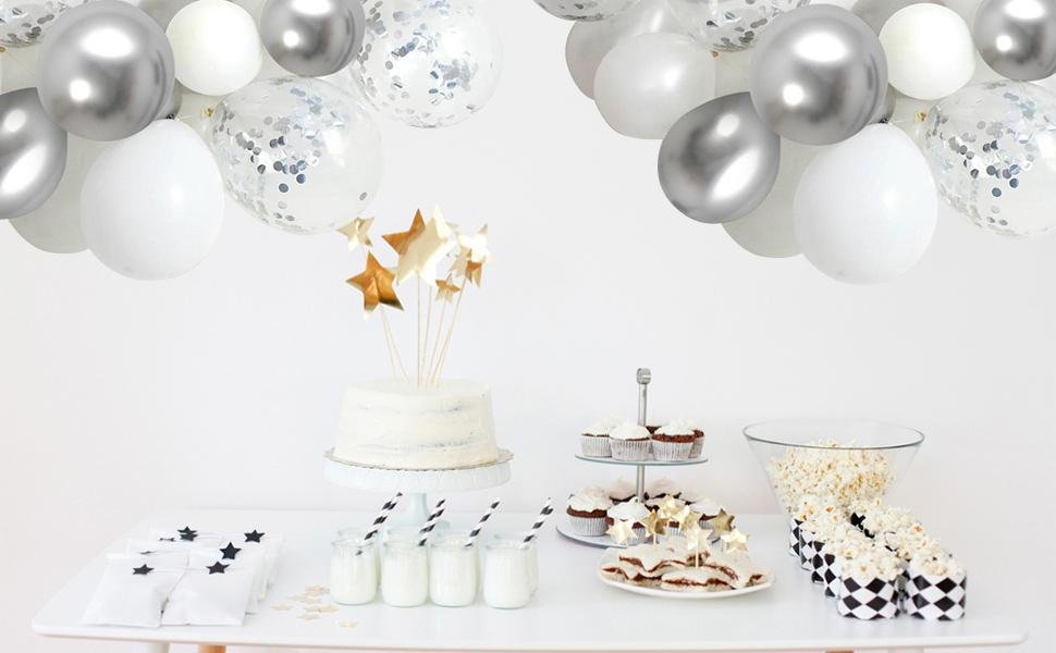 Party table with white cake, cupcakes, popcorn, and white and silver balloons overhead