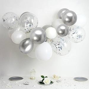 White and silver confetti balloons arranged in a garland, with a small table setting below.