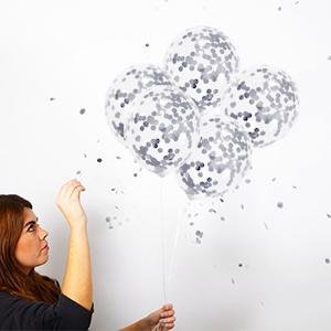 Woman holding a bunch of clear confetti balloons with silver glitter against a white wall