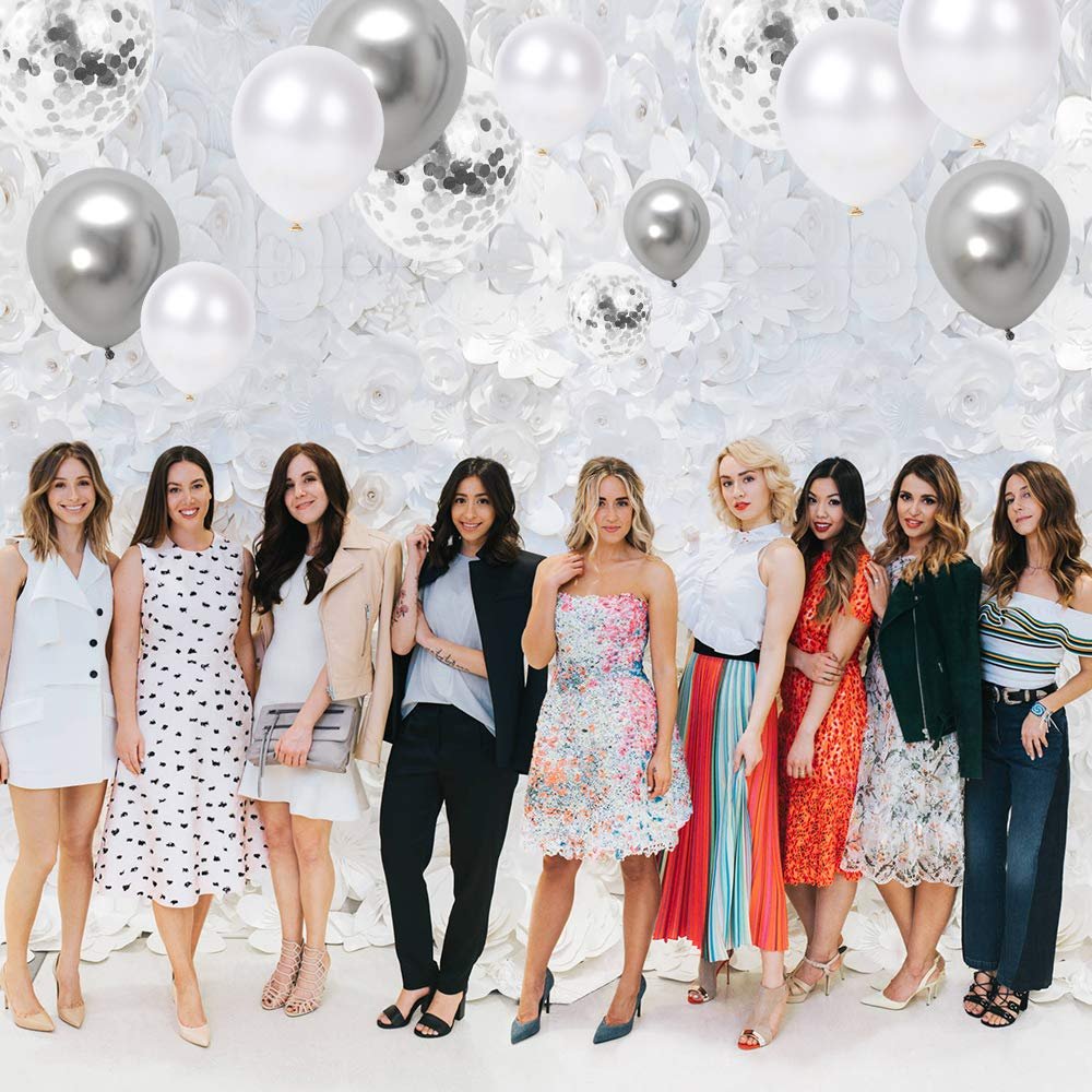 Group of eight women posing in front of a white floral wall with silver and white balloons