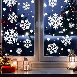 White snowflake window clings applied to a dark window with a Christmas tree and lights visible outside.