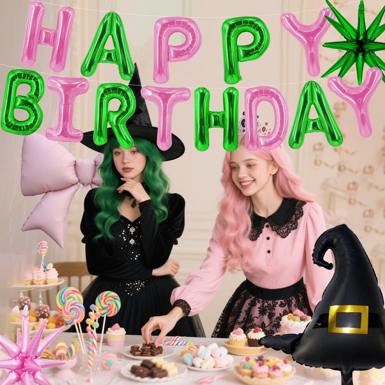 Two women in witch costumes at a party table with pink and green happy birthday balloons and sweets
