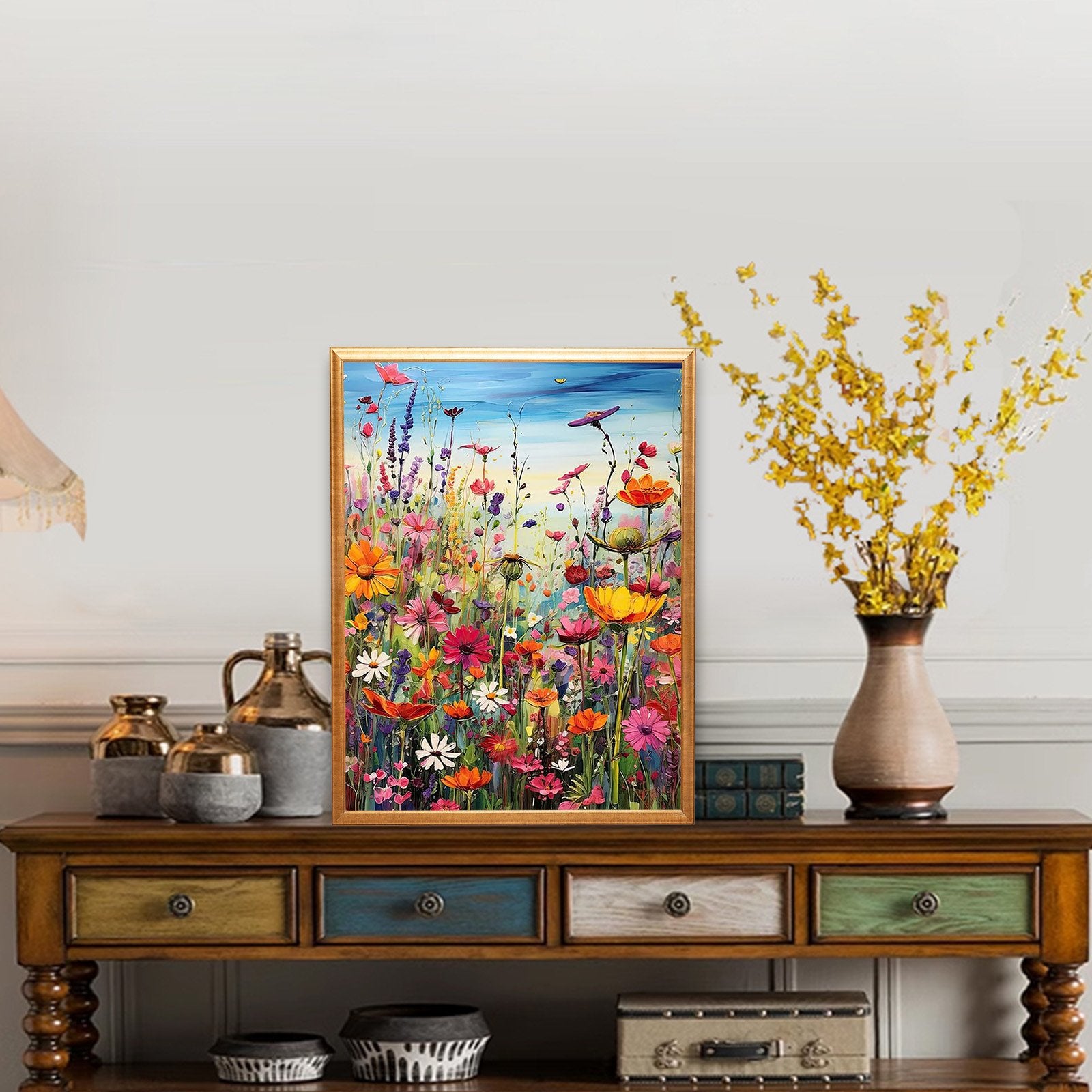 Framed painting of a vibrant field of wildflowers displayed on a wooden console table with decorative vases and books.