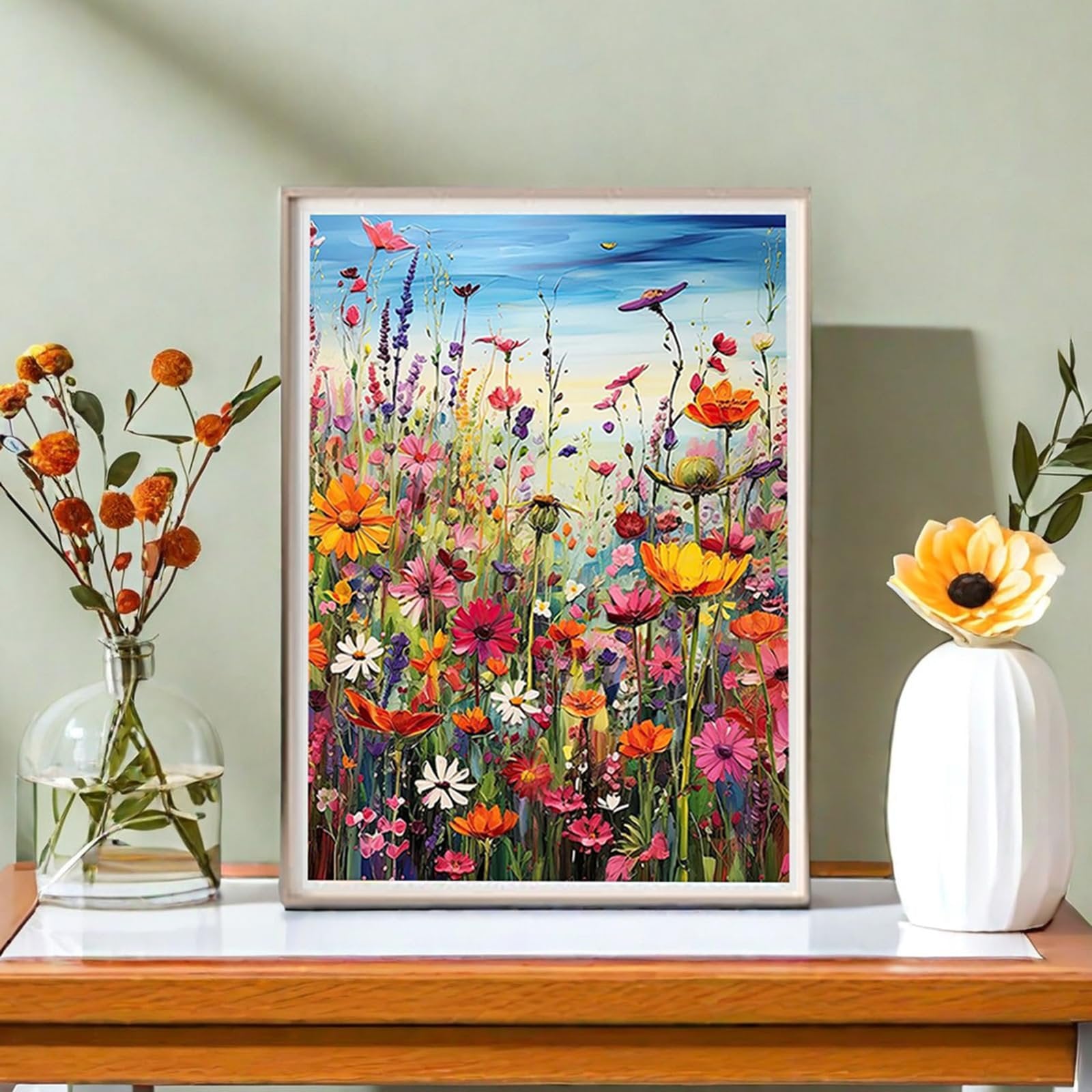Framed painting of a vibrant field of wildflowers under a blue sky, displayed on a shelf with vases of flowers.