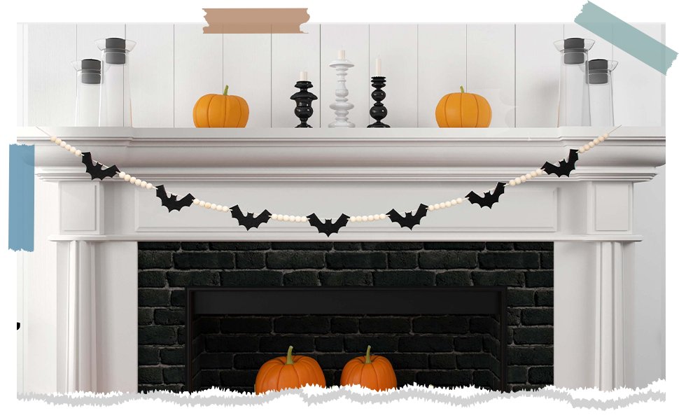 Halloween garland with black felt bats and wood beads draped across a fireplace mantel with pumpkins and candlesticks