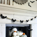 Halloween bat and wood bead garland draped over a fireplace mantel with pumpkins below