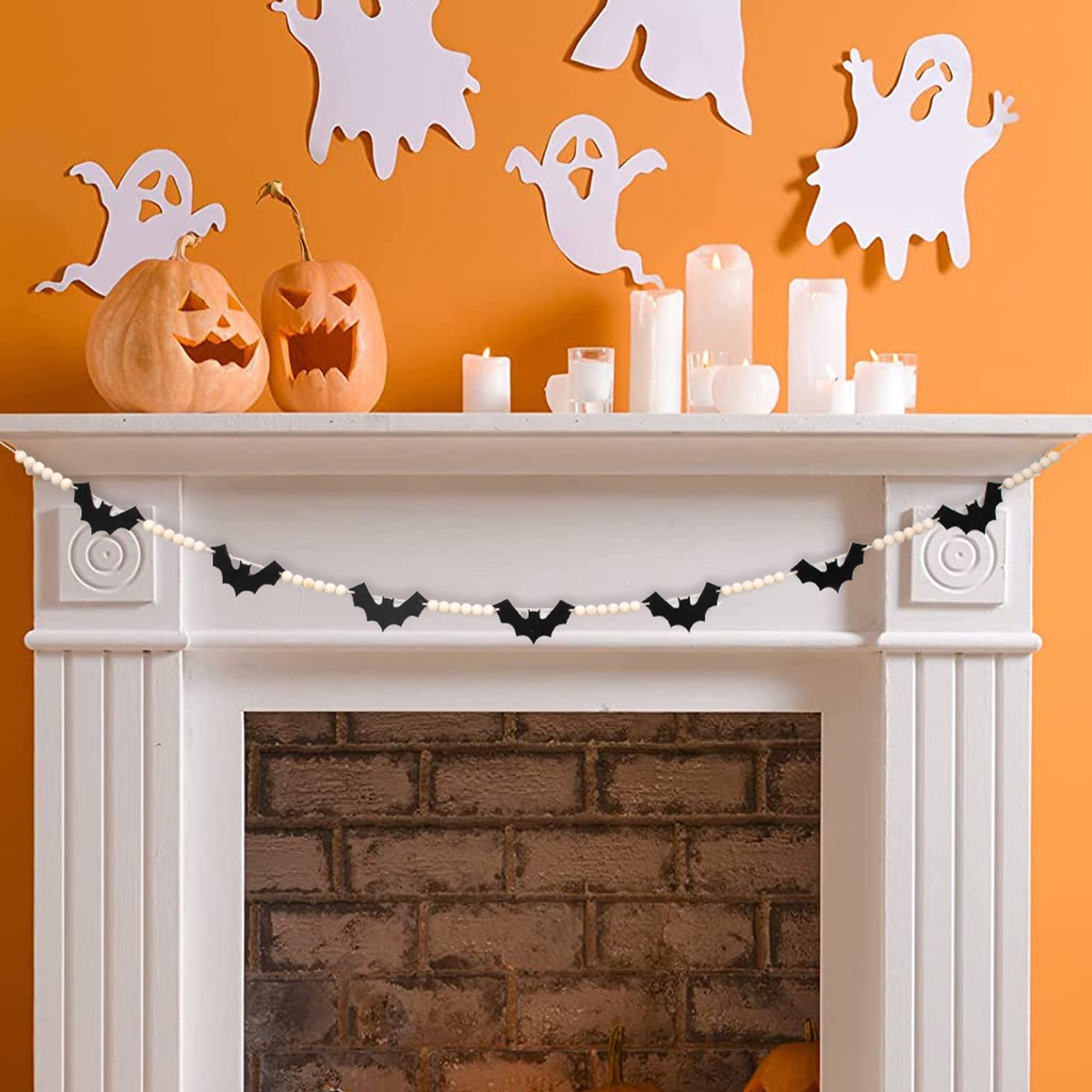 Halloween garland with black felt bats and wood beads draped across a fireplace mantel with carved pumpkins and candles