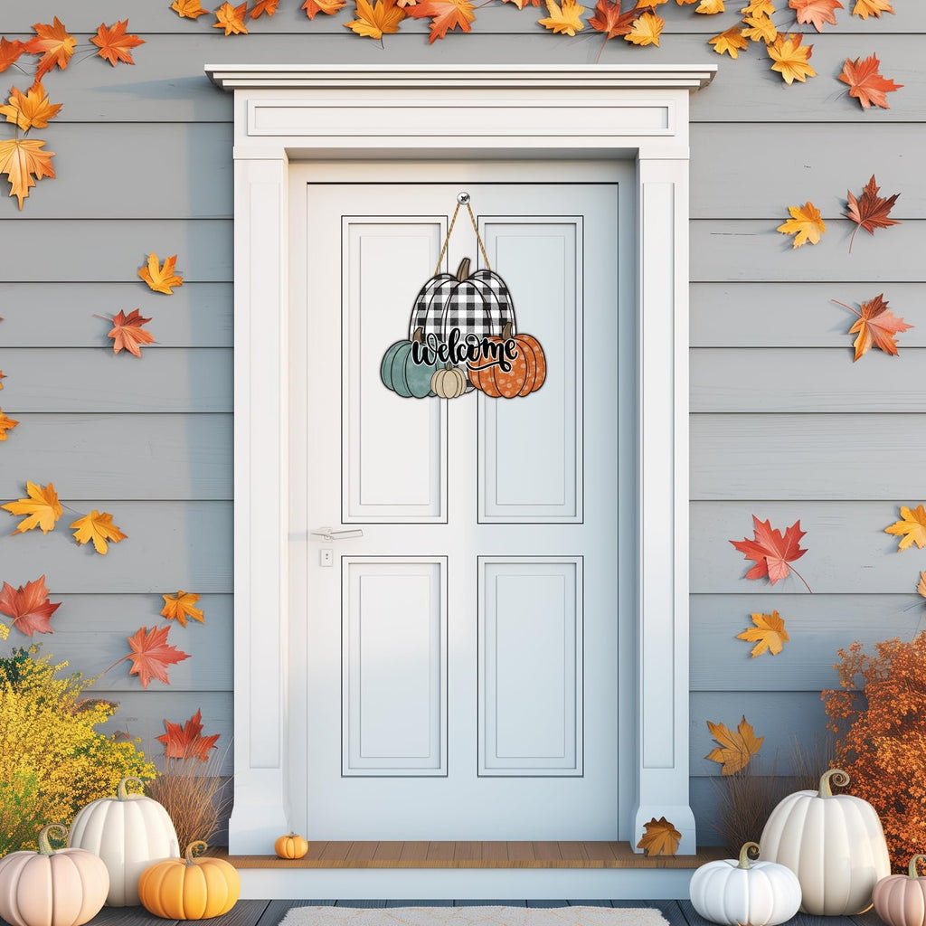 Wooden pumpkin welcome sign with buffalo plaid and fall leaves hanging on a white door.