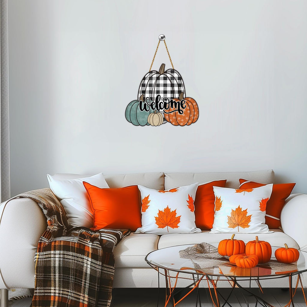 Hanging wooden pumpkin sign with buffalo plaid and 'welcome' text, displayed above a sofa with fall-themed pillows and a blanket.