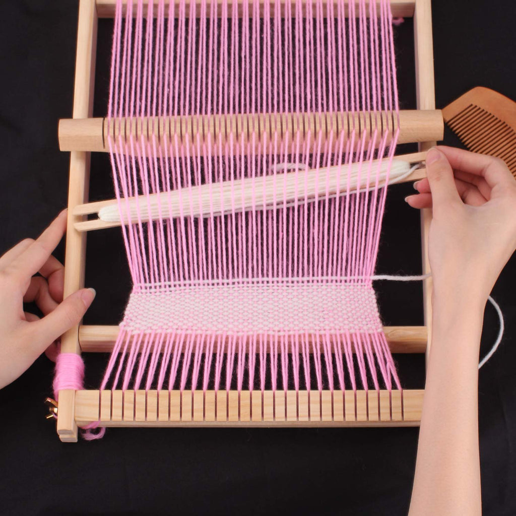 Hands weaving pink yarn on a wooden loom frame with a comb and shuttle