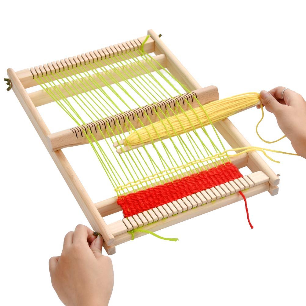 Wooden weaving loom with green and red yarn being woven, hands holding shuttle and adjusting loom.