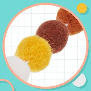 Close-up of a wool felt pom pom garland with balls in white, yellow, brown, and orange against a grid background and teal border.