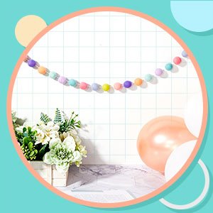 Wool felt pom pom garland in pastel colors strung across a grid background, with flowers and balloons.