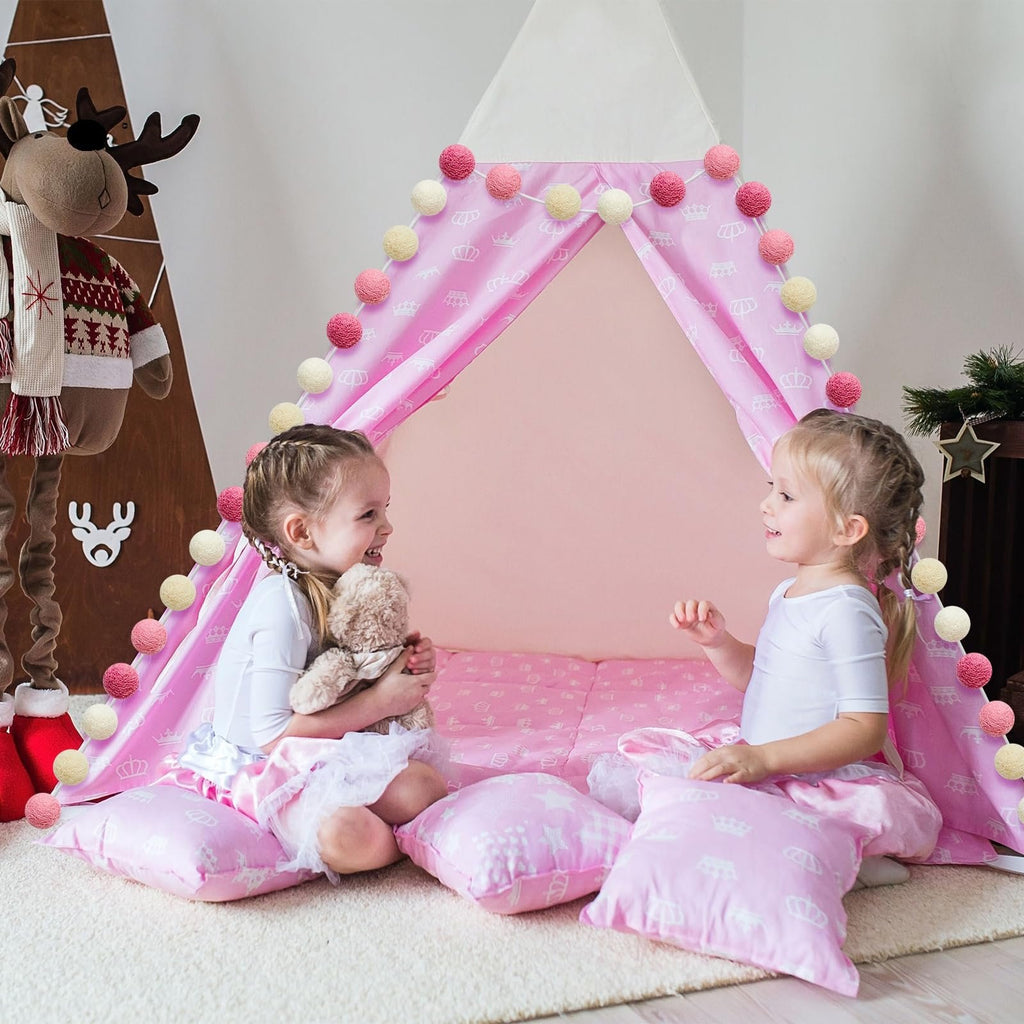Two young girls playing inside a pink tent decorated with pom pom garlands and crown patterns.