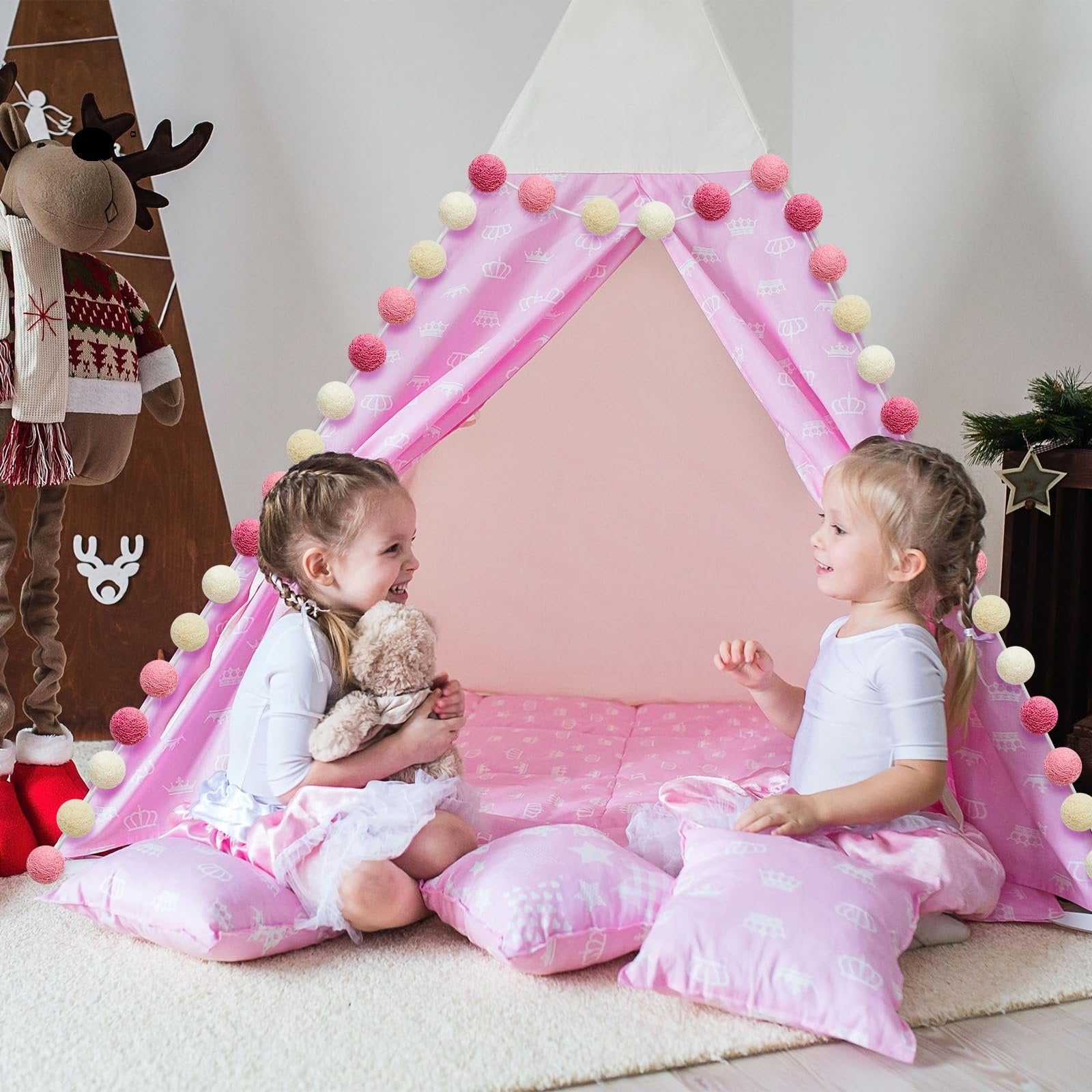Two young girls playing inside a pink tent decorated with pom pom garlands and crown patterns.
