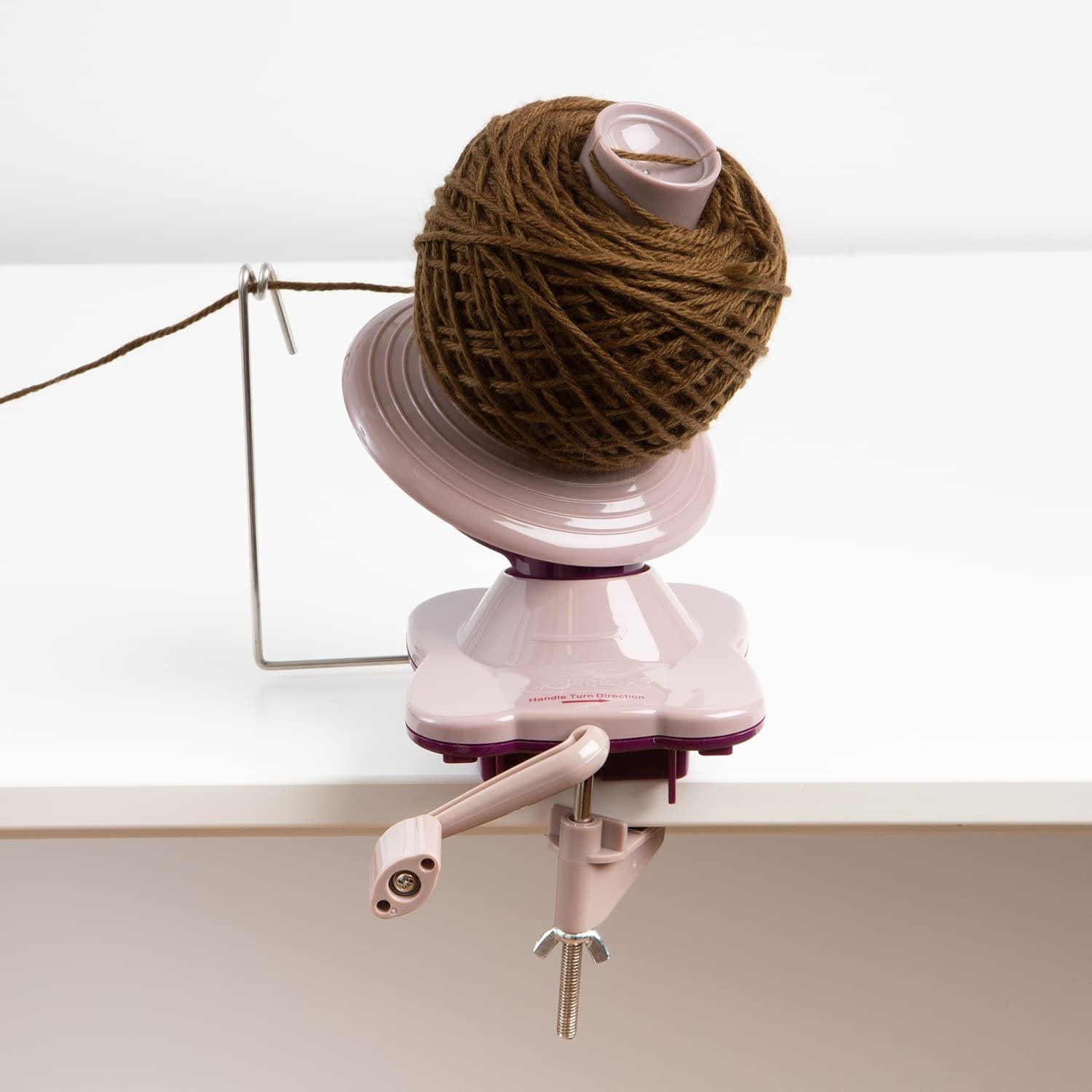 Yarn ball winder with brown yarn attached, clamped to a white surface.